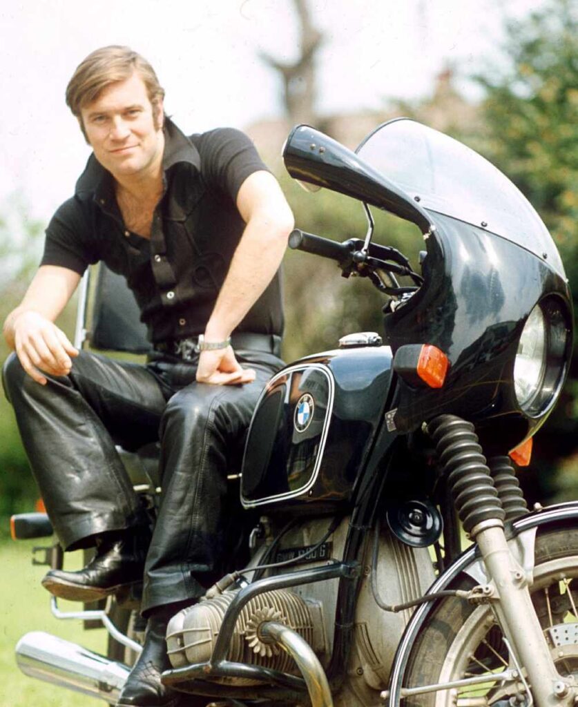 Nicky Henson sitting on a motorcycle.