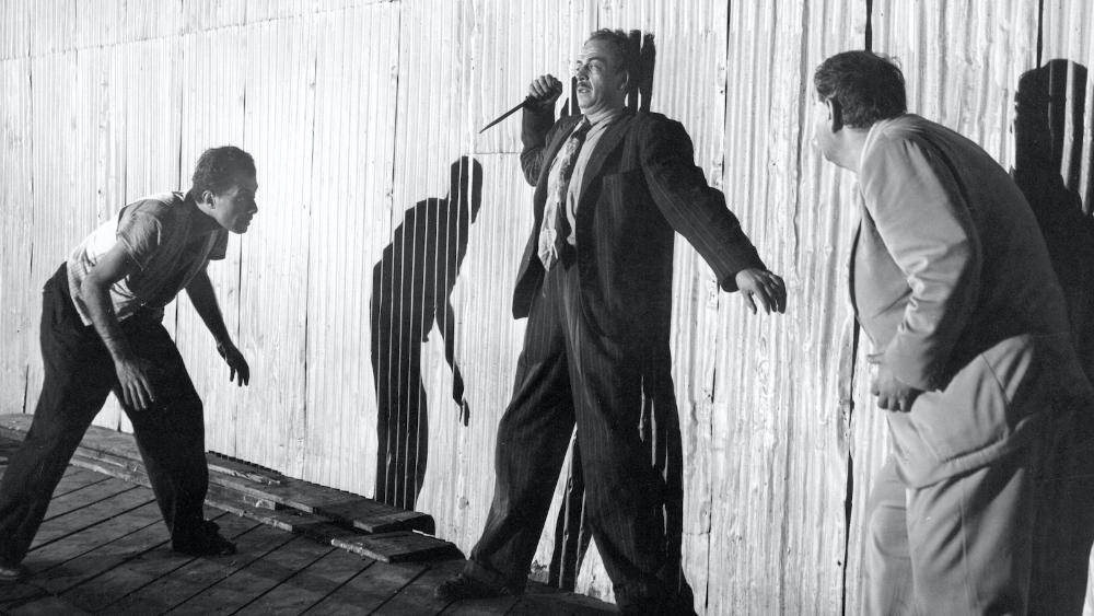 Panic in the Streets. Man with knife backed against a wall and two people moving in on him.